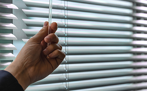 a person adjusting venetian blinds to adjust the light going into a room