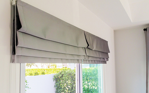 grey roman blinds pulled up against a window